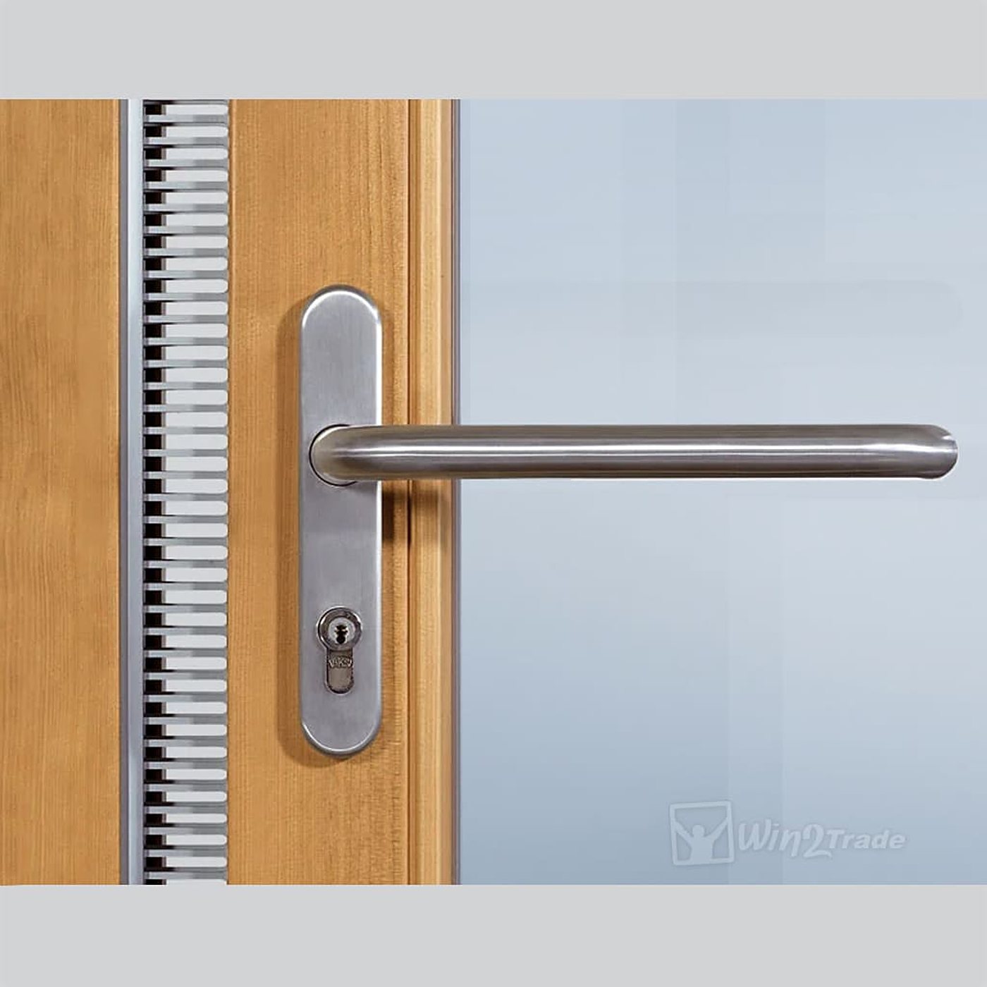 Gros plan d'une poignée en inox brossé avec serrure à cylindre sur une porte en bois clair, à côté d'une grille de ventilation et d'un panneau vitré.